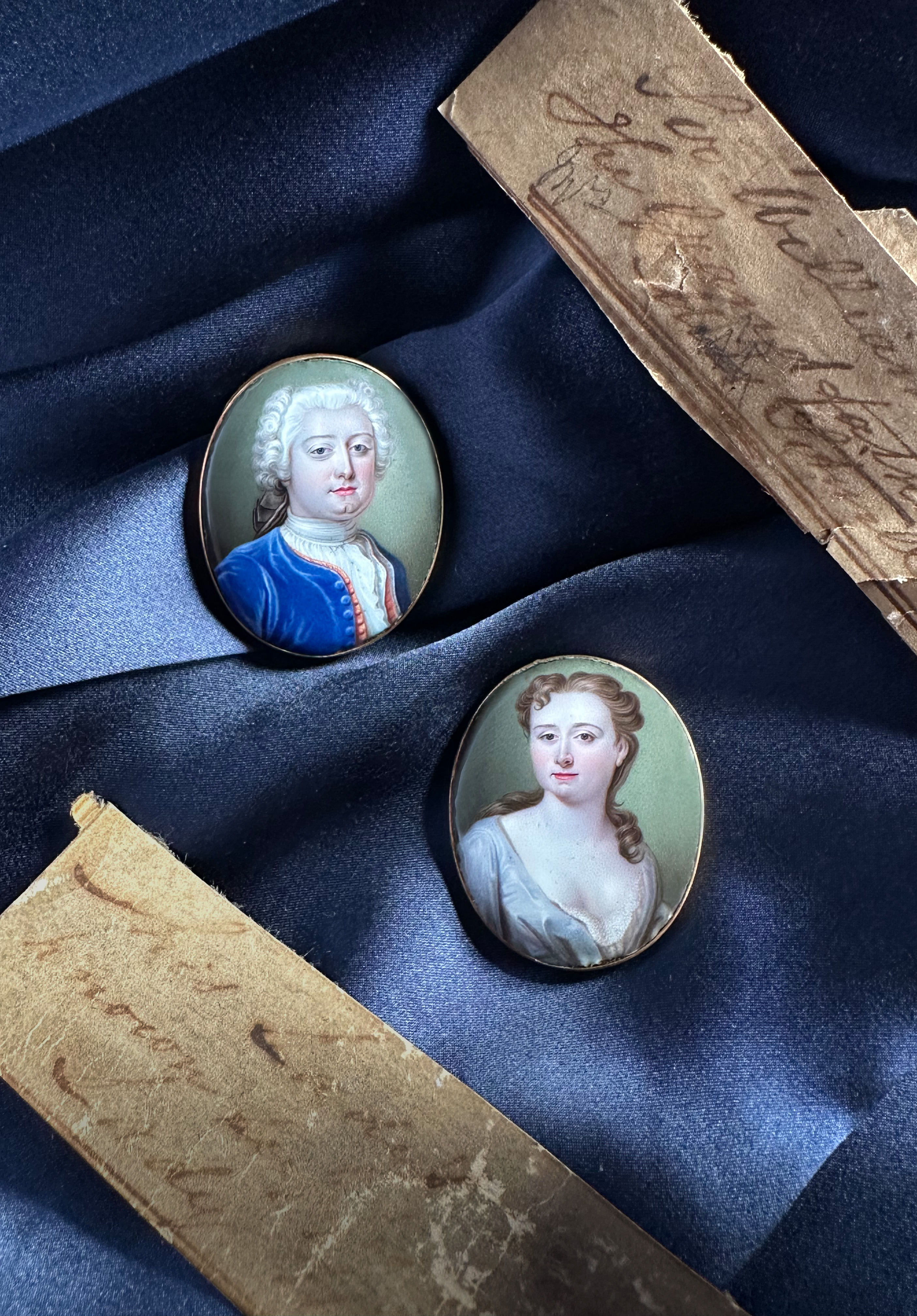 Pair of portrait enamels of husband and wife Sir William Wheler (1702-1763), 5th Bart of the City of Westminster and Lady Penelope Wheler (née Glynne) (1706-1740); he wearing blue coat and red waistcoat; she in white open-fronted gown with lace underdress