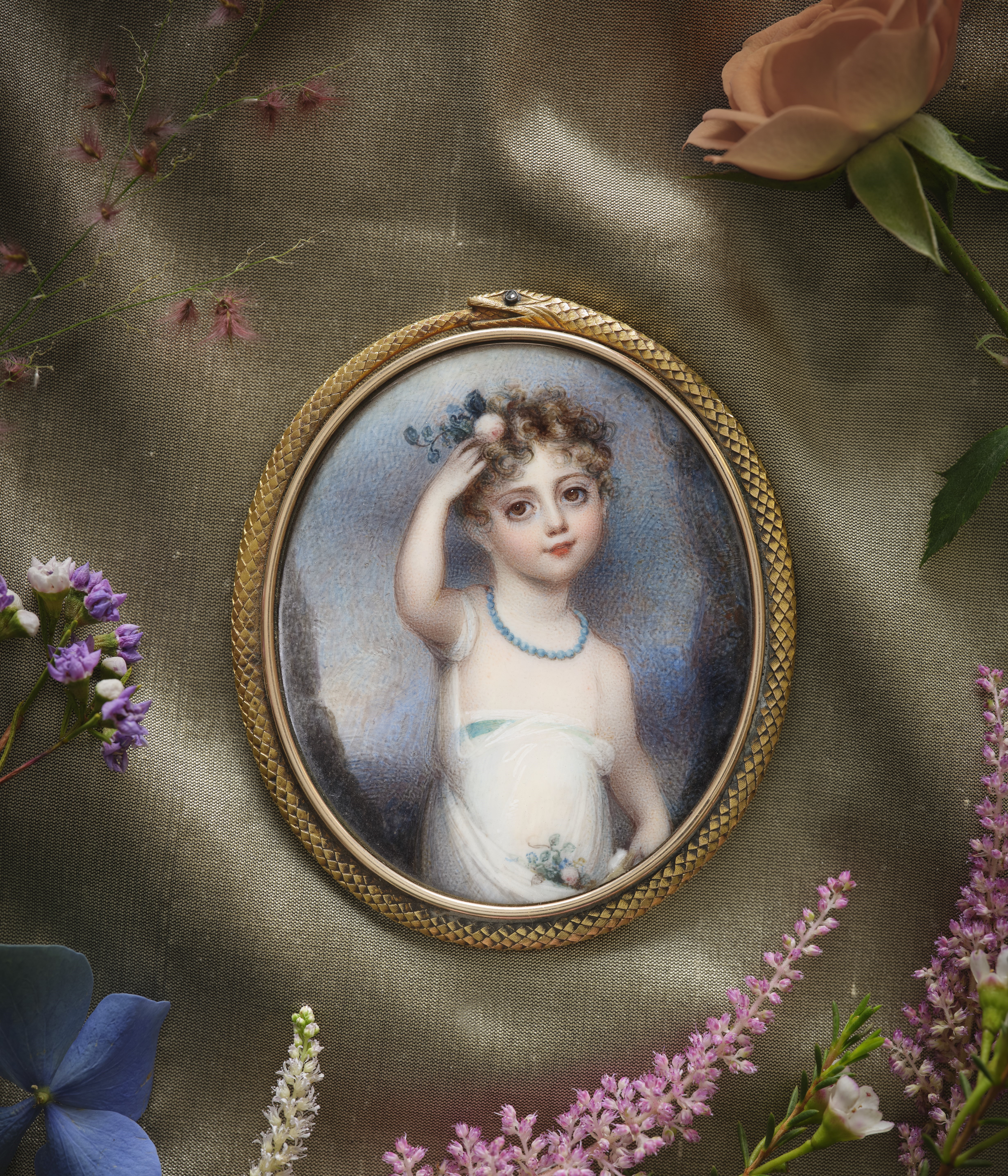 Portrait miniature of a Child, wearing white gown, holding flowers to their curled hair and in their skirt, landscape background