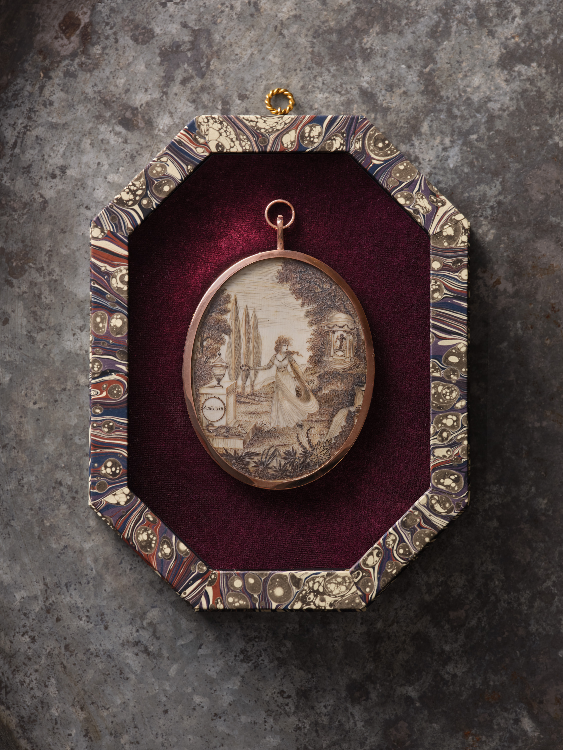 A double-sided hairwork miniature, the front decorated with a couple in a garden, with ‘Je me tache ou je meurs’ inscribed on a pedestal, also decorated with two flaming hearts, the pedestal surmounted by a cupid, the other with a woman fleeing through a garden, with ‘Amicizia’ inscribed on a pedestal