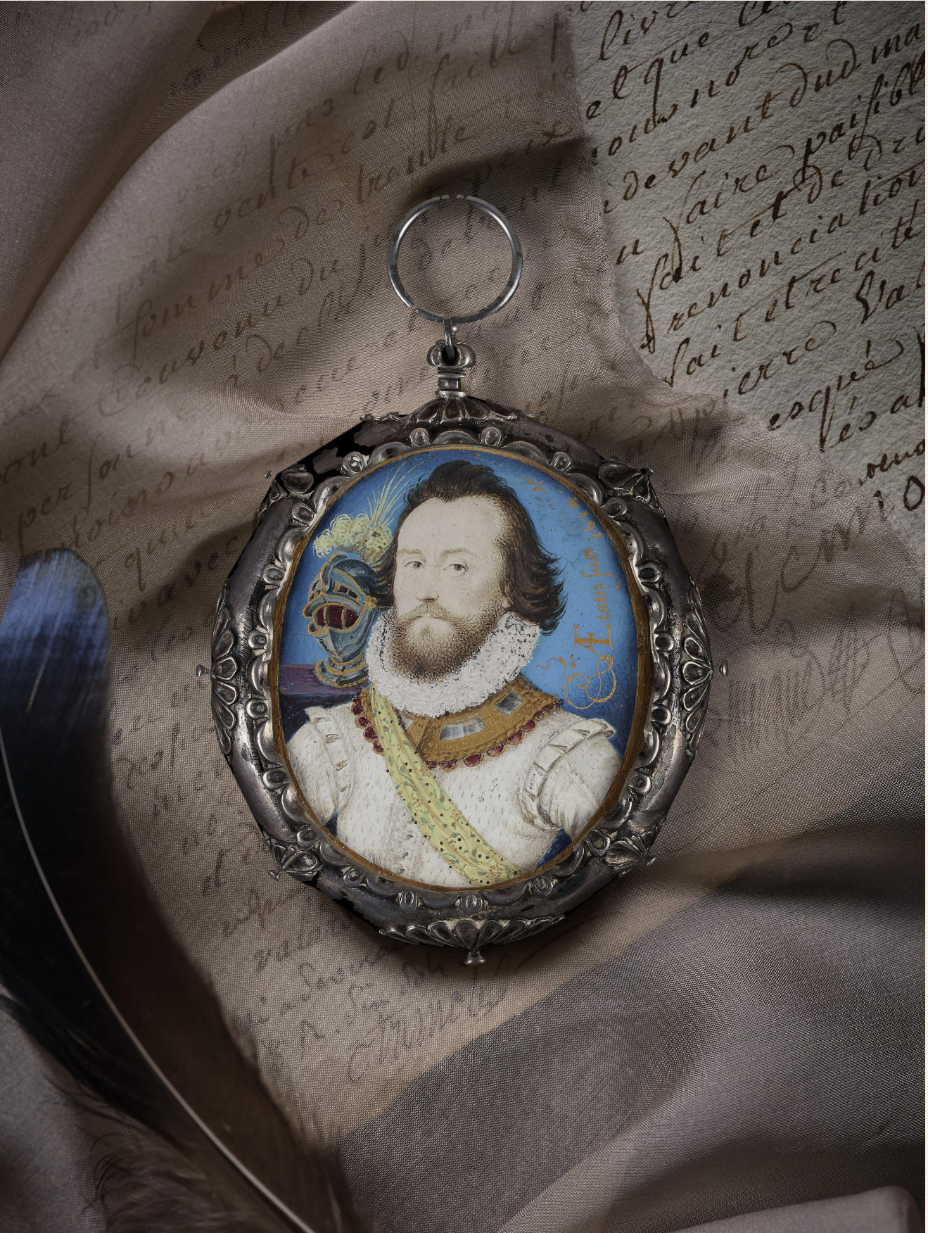 Portrait miniature of a Soldier, wearing white doublet and ruff, jewel-set gorget, yellow embroidered sash and gilt-banded helmet with white plumes on a purple velvet plinth behind; gold calligraphy ‘Ӕtatis Suӕ [...] 1614'