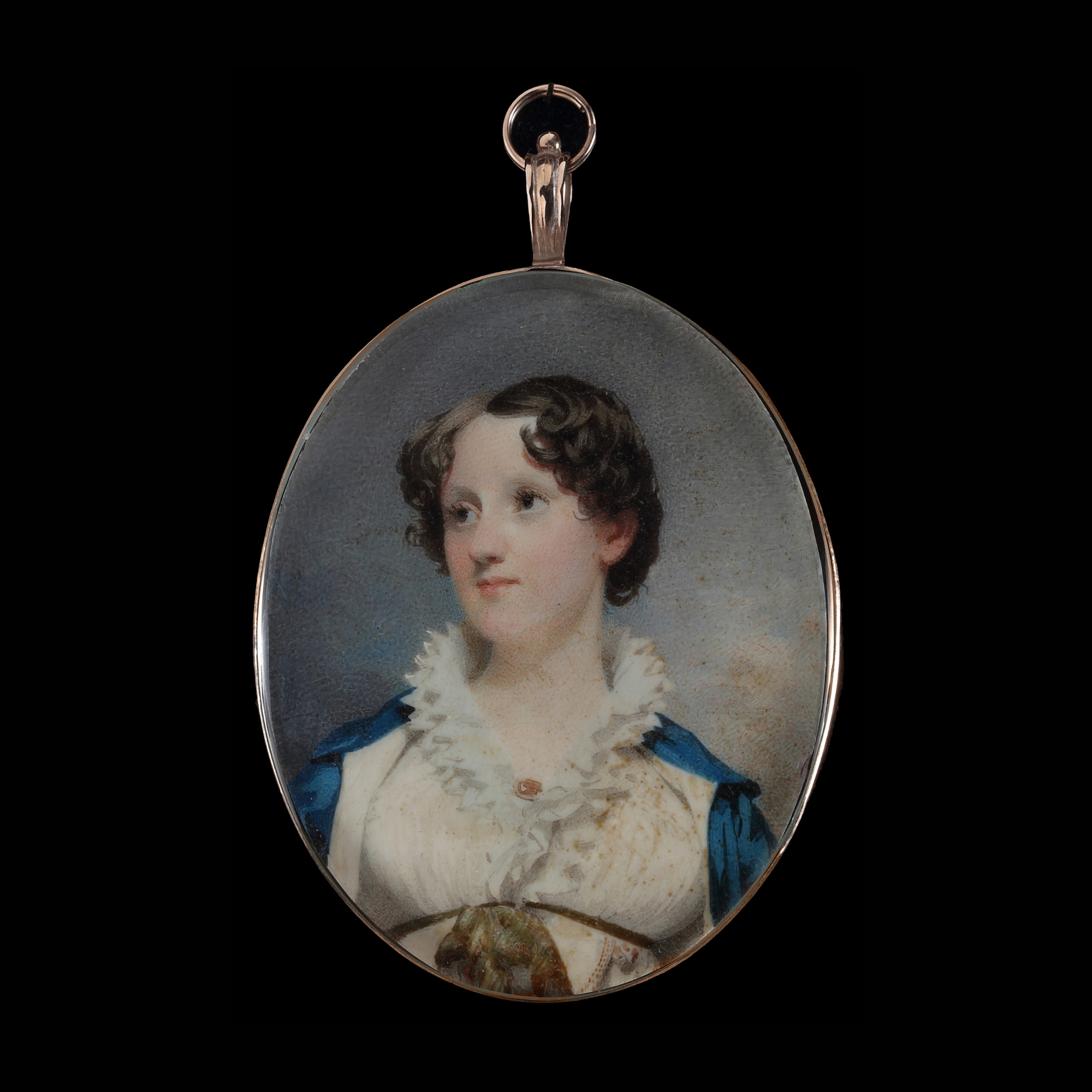 Portrait miniature of a Young Lady, wearing cream dress with white frilled collar and brooch, a green ribbon under her bust and cream-lined blue cloak, circa 1810